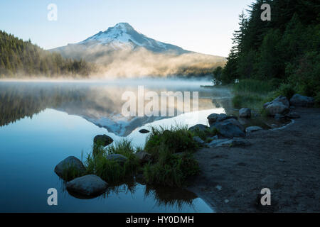 Trillium lake sits perfectly calm displaying a smooth reflection of Mt. Hood with a layer of fog around its base Stockfoto