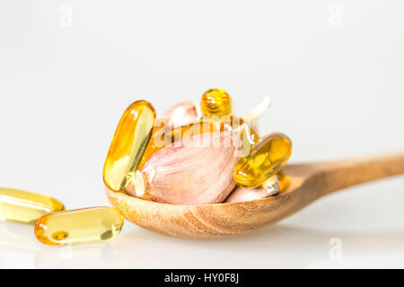 Knoblauch und Öl Kapsel Gel Ergänzung in einem Holzlöffel auf weißem Hintergrund, gesunde Vitamin-Ergänzung von Knoblauch Öl Konzept hautnah Stockfoto