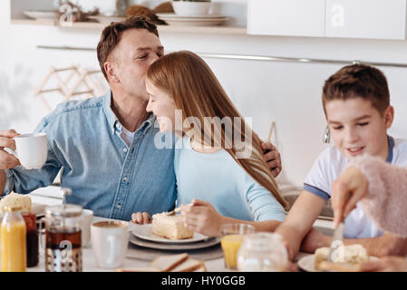 Bringen Sie Ihre Liebe zum Ausdruck. Fröhliche liebender Vater seine Tochter küssen, während Sie am Tisch sitzen und Essen zu Hause genießen Stockfoto