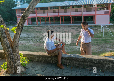 Zwei Schüler im Chat auf dem Campus einer Grundschule in Phuket, Thailand. Stockfoto