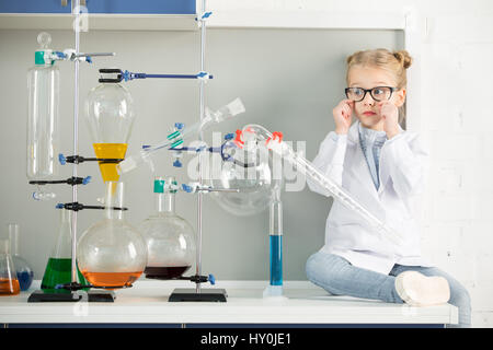 Kleines Mädchen im weißen Kittel und Brillen auf Tisch im Wissenschaftslabor Stockfoto