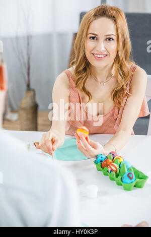 Junge Frau bemalen von Ostereiern und lächelt in die Kamera Stockfoto