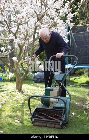 Rentner, die versuchen, starten Sie einen Benzin-Rasenmäher in einem englischen Wohn Garten auf einer Feder Nachmittag, Surrey, England, Vereinigtes Königreich Stockfoto