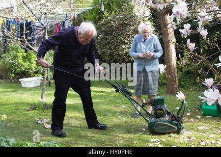 Rentner, die versuchen, starten Sie einen Benzin-Rasenmäher in einem englischen Wohn Garten auf einer Feder Nachmittag, Surrey, England, Vereinigtes Königreich Stockfoto