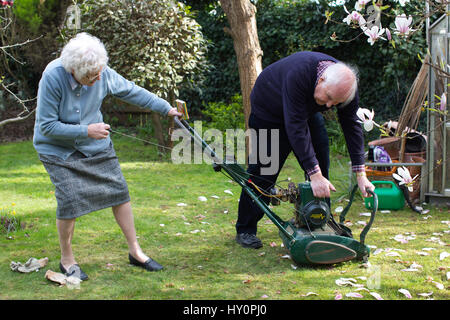 Rentner, die versuchen, starten Sie einen Benzin-Rasenmäher in einem englischen Wohn Garten auf einer Feder Nachmittag, Surrey, England, Vereinigtes Königreich Stockfoto