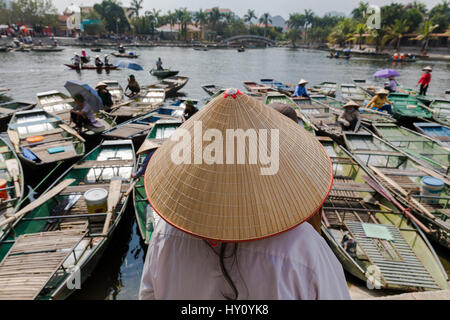 Nicht identifizierte Vietnamesin mit Blick auf ihre Boote tragen traditionelle vietnamesischen Strohhut in Ninh Binh, Tam Coc Wharf. Stockfoto