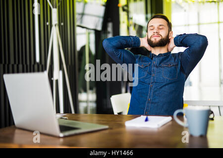 Junger Geschäftsmann entspannend an seinem Schreibtisch im Büro Stockfoto