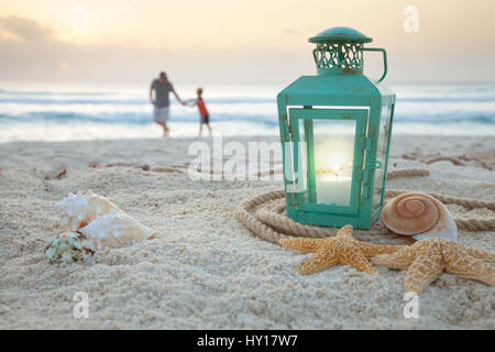 Laterne mit Muscheln am Strand mit soft-Focus-Vater und Sohn sammeln von Muscheln im Hintergrund bei Sonnenaufgang Stockfoto