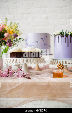 Vertikales Bild von Cupcakes auf einem Stand mit Kuchen und Blumen im Hintergrund. Stockfoto