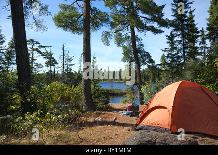 Ein Campingplatz mit einem orangefarbenen Zelt und Koch-Ofen mit Blick auf eine Boundary Waters-See im Norden von Minnesota Stockfoto