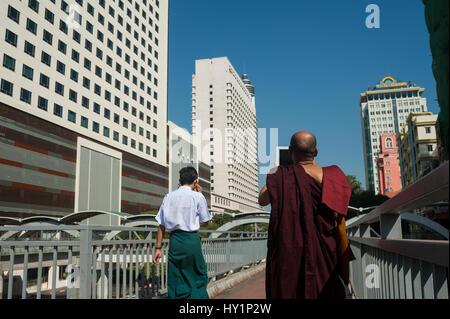 27.01.2017, Yangon, Republik der Union Myanmar, Asien - ein buddhistischer Mönch steht auf einer Fußgängerbrücke und nimmt Bilder der neuen sule Square. Stockfoto