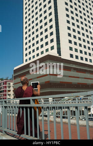 27.01.2017, Yangon, Republik der Union Myanmar, Asien - ein buddhistischer Mönch steht auf einer Fußgängerbrücke und nimmt Bilder der neuen sule Square. Stockfoto