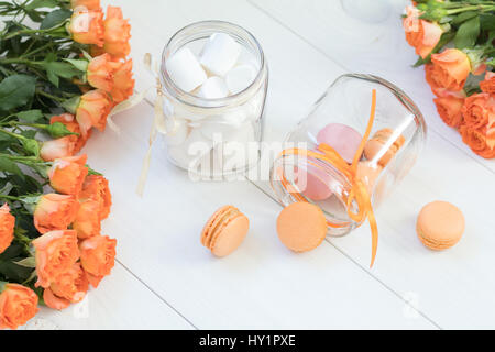 Orange-Mango oder citrous Makronen und Marshmallow in Gläsern. Frische kleine Rosen. Hellen Holz Hintergrund. Sonnenlicht. Färbung und Verarbeitung Foto mit l Stockfoto