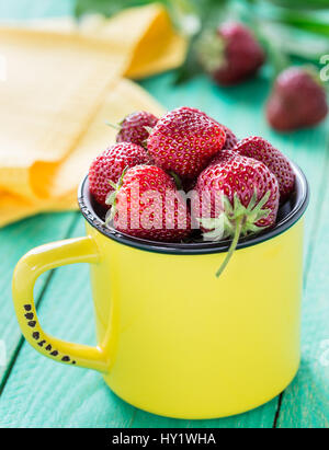Frische Erdbeeren in eine gelbe Tasse auf Holztisch Stockfoto