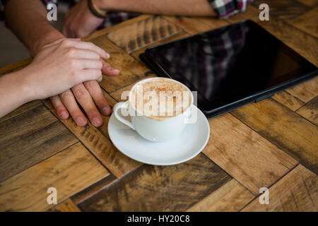 Bild von paar Hand in Hand mit Kaffeetasse und Tablet-PC auf Tisch im Café beschnitten Stockfoto