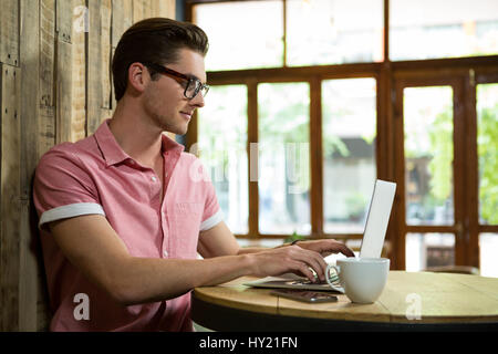 Seitenansicht des gut aussehenden jungen Mann mit Laptop am Tisch im Café Stockfoto