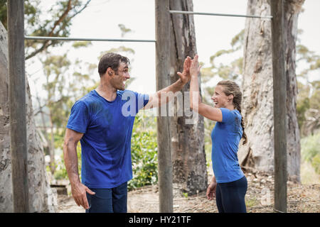 Lächelnder Mann und Frau geben hohe fünf während der Hindernis-Parcours mit Boot camp Stockfoto