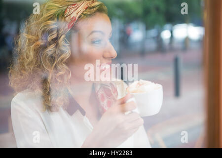 Nahaufnahme der jungen Frau trinken Kaffee in der Cafeteria gesehen durch Fenster Stockfoto