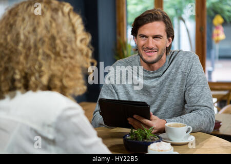 Junger Mann mit Tablet-PC beim betrachten Frau in Coffee-shop Stockfoto
