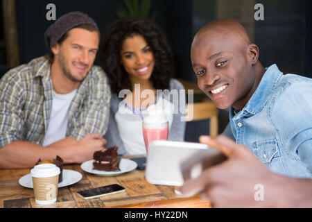 Glücklicher Mann mit Freunden nehmen Selfie am Holztisch in Coffee-shop Stockfoto