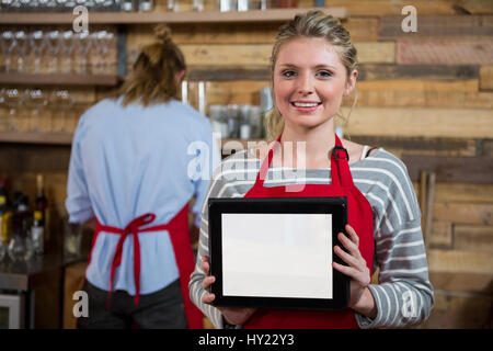 Porträt der lächelnde junge Frau zeigt digital-Tablette mit männlichen Kollegen im Hintergrund im Coffee shop Stockfoto