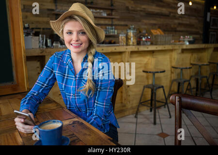 Porträt der jungen Frau mit Hut im Coffee-Shop mit gedrückter Handy Stockfoto