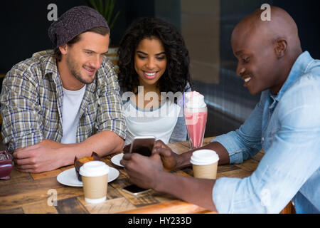 Junger Mann mit Handy an Freunde am Tisch im Café Stockfoto