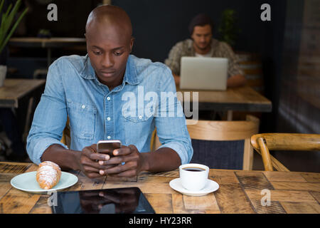 Junger Mann mit Handy am Holztisch in Coffee-shop Stockfoto