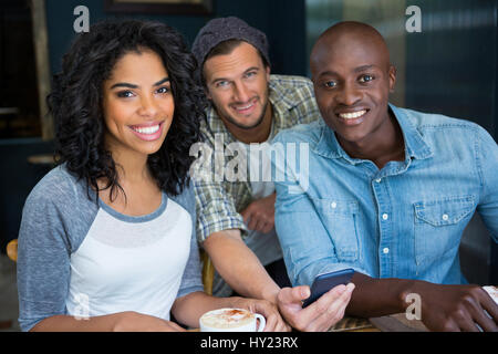 Porträt von Multi ethnischen männliche und weibliche Freunde mit Handy in Coffee-shop Stockfoto