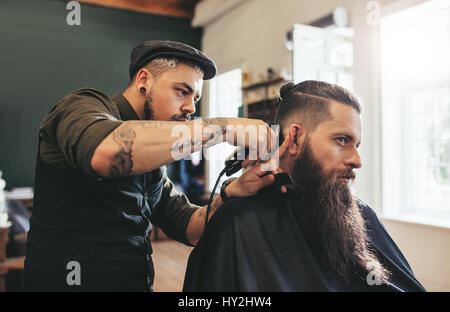 Hübscher Junge bärtige kaukasischen Mann immer trendigen Haarschnitt im Barbershop. Friseur servieren Kunden im Salon. Stockfoto