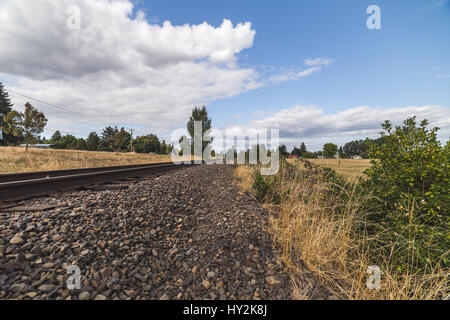 Geschwollene weiße Wolken schweben in einem lebhaften blauen Himmel über dem Zug verfolgt im ländlichen Oregon, USA. Stockfoto