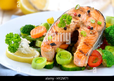 Lecker gegrilltes Lachssteak auf bunten Gemüse, Zitronen und ein Fischernetz im Hintergrund Stockfoto