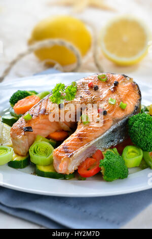 Lecker gegrilltes Lachssteak auf bunten Gemüse, Zitronen und ein Fischernetz im Hintergrund Stockfoto