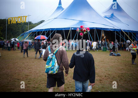 Menschen wandern in den Schlamm halten einen Regenschirm mit rosa Blüten, Green Man-Festival, Wales Stockfoto