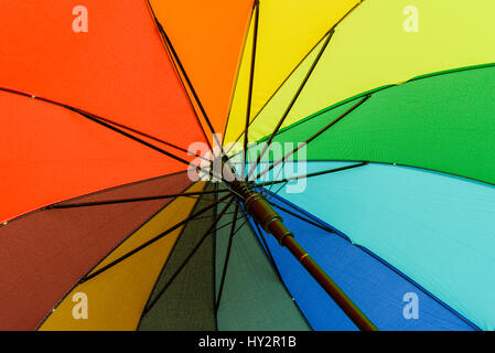 Multi farbige Schirm, die ihre Benutzer vor Regen unter dem Regenbogen farbige Segmente schützt Stockfoto