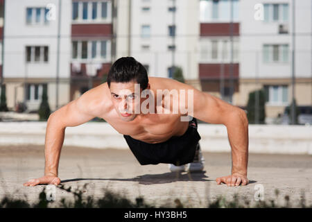 Porträt von starken jungen Athleten Push-uping im Freien im Hof Stockfoto