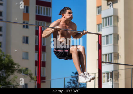 Passen junge Mann tut Push Ups auf horizontale Leiste im Freien mit großem Aufwand. Stockfoto