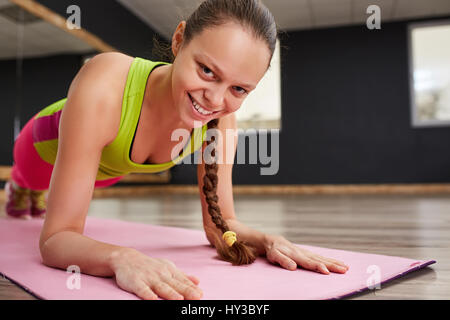 Porträt einer lächelnden jungen sportlichen Frau stretching Hände auf rosa Gymnastikmatte Stockfoto