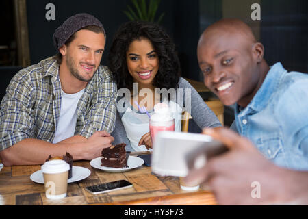 Glücklich Jüngling mit Freunden nehmen Selfie am Holztisch in Coffee-shop Stockfoto