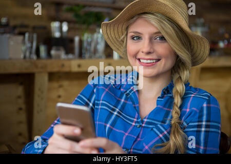 Porträt der lächelnde junge Frau Hut mit Handy in Coffee-shop Stockfoto