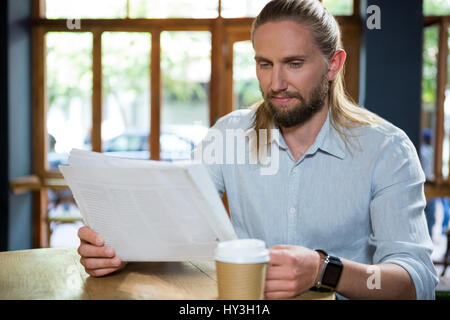 Hübscher junger Mann liest Zeitung am Tisch im Café Stockfoto