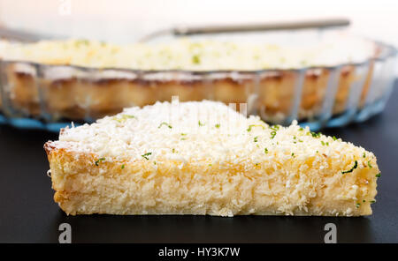 Zitrone, Limette, Kokosnuss unmöglich Torte mit weißer Schokolade Späne Scheibe mit Auflaufform im Hintergrund Stockfoto