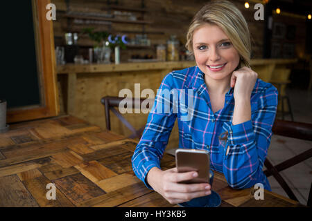Porträt der lächelnde junge Frau mit Handy am Tisch im Café Stockfoto