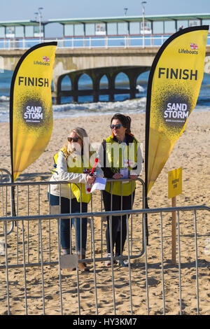 RNLI Rettungsschwimmer Marshalls am Briefing Zone beende Post der Sandsturm Beach Challenge, am Strand von Bournemouth, ein Strand-Hindernisparcours im März Stockfoto