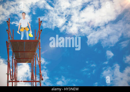 Glücklich Mechaniker mit Wasserwaage und Bauarbeiterhelm gegen Blick auf schönen Himmel und Wolken Stockfoto