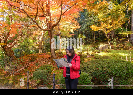 Frau Tourist in rote Jacke und mit Kamera steht und schaut auf die Karte im Garten mit herbstlichen Farbe Bäume im Shisen-Do-Tempel Stockfoto