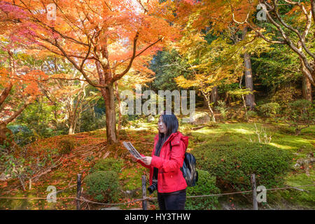 Frau Tourist in rote Jacke und mit Kamera und Karte steht und sieht im Garten mit herbstlichen Farbe Bäume in Shisen-Do Templ Stockfoto