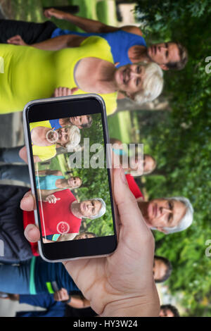 Hand halten Handys vor weißem Hintergrund gegen Marathon Athletinnen und Athleten laufen Stockfoto