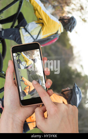Hände berühren Smartphone gegen Seitenansicht der Biker paar Fahrrad Natur Stockfoto