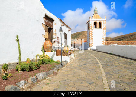 Dorfstraße mit traditionellen Häusern mit Blumentöpfen vor und Turm der Kathedrale Santa Maria de Betancuria in Betancuria Seilbahn Hintergrund Stockfoto